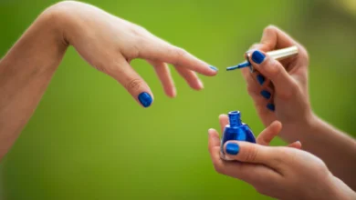 Mulher aplicando esmalte vegano azul em outra mulher em ambiente natural.