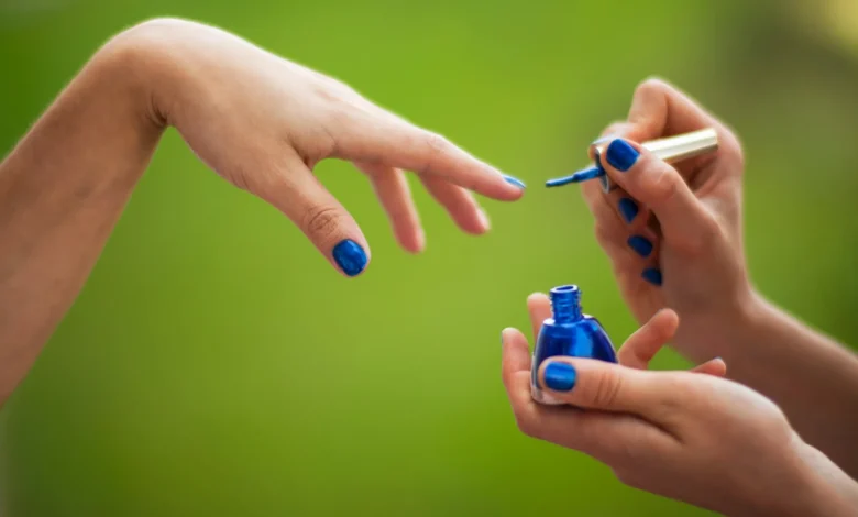 Mulher aplicando esmalte vegano azul em outra mulher em ambiente natural.