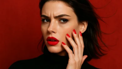 Imagem de uma mulher com unhas e lábios vermelhos, olhando com expressão intrigada. A foto é focada na manicure de esmalte vermelho, tema inverno.