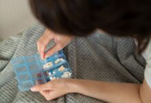 Mãos organizando comprimidos em caixa semanal de medicamentos