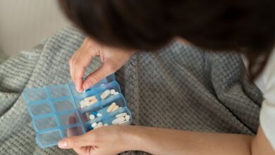 Mãos organizando comprimidos em caixa semanal de medicamentos