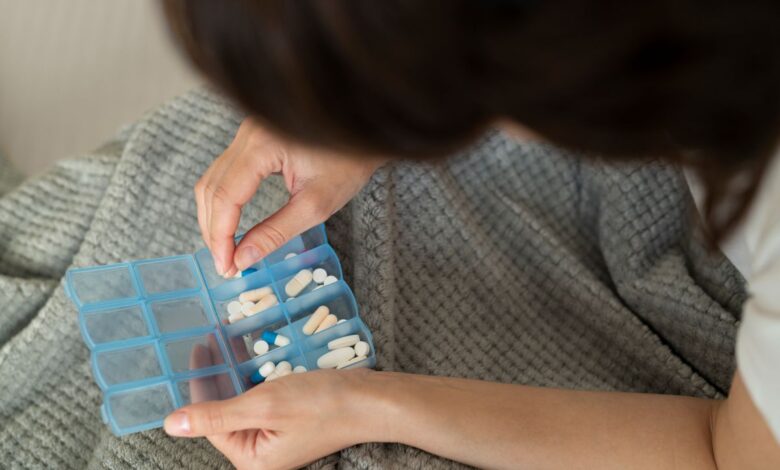 Mãos organizando comprimidos em caixa semanal de medicamentos