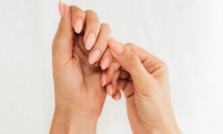 Mãos femininas com unhas alongadas, esmaltadas e bem cuidadas em tom nude