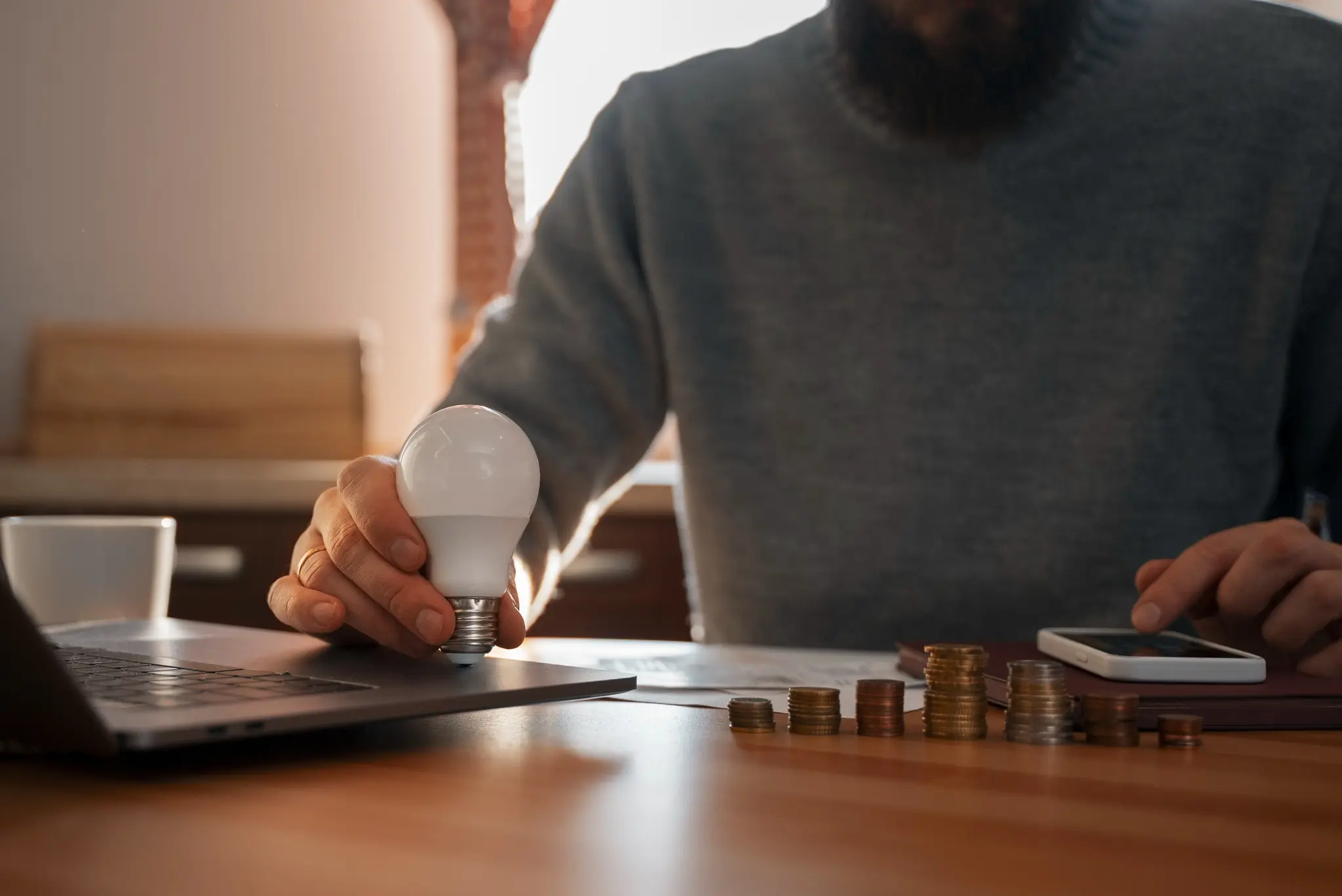 Homem segurando lâmpada e economizando energia enquanto usa um laptop, ilustrando como obter empréstimos na conta de luz