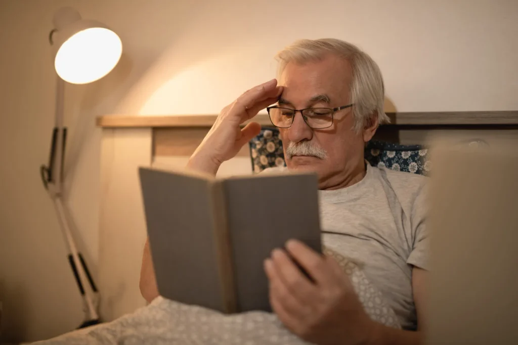 Homem idoso lendo um livro à noite na cama, focado em melhorar a memória com dicas importantes para a terceira idade.