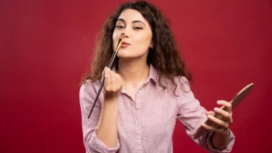 Mulher jovem aplicando maquiagem com pincel em um fundo vermelho, demonstrando técnica de maquiagem