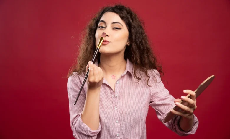 Mulher jovem aplicando maquiagem com pincel em um fundo vermelho, demonstrando técnica de maquiagem
