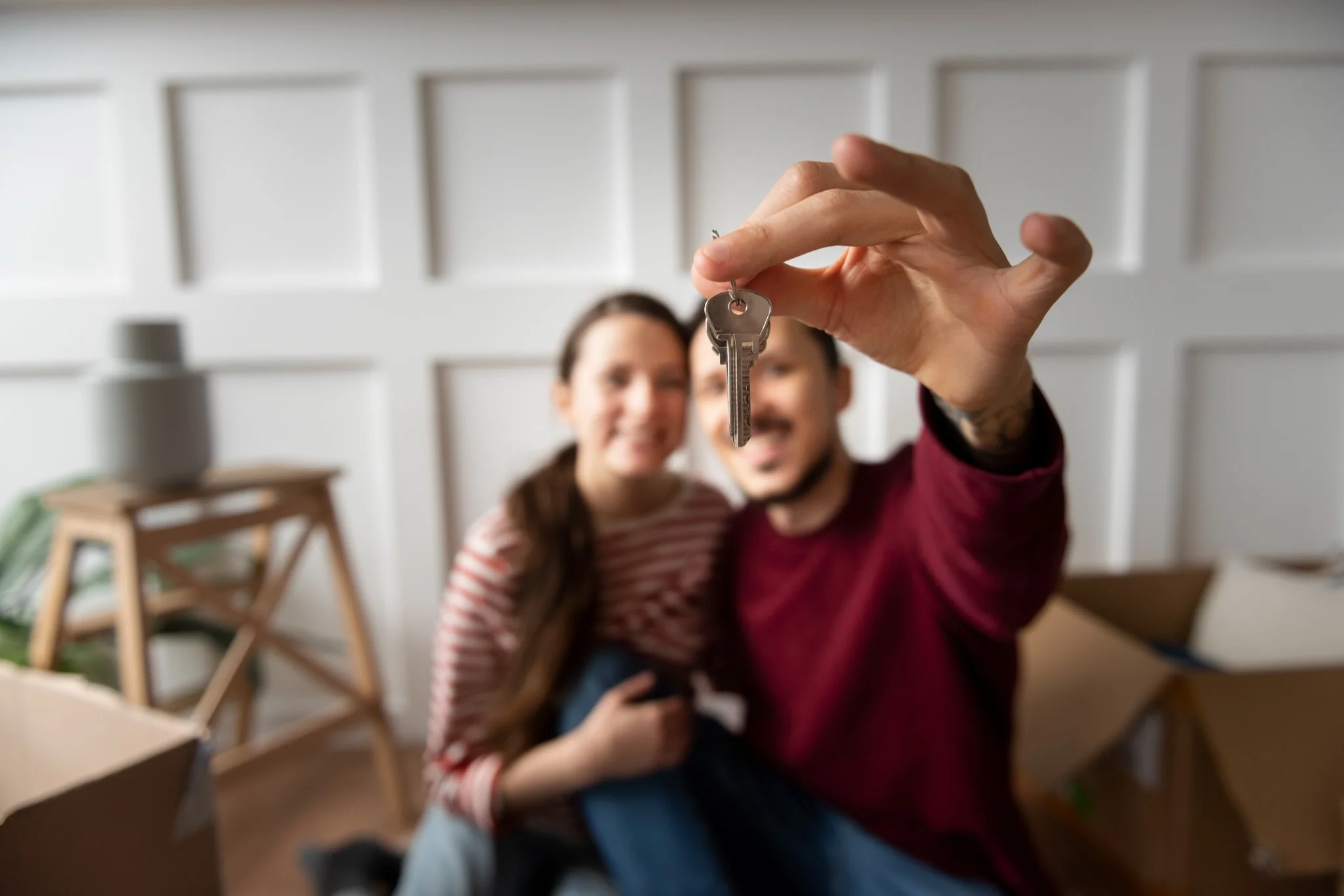 Casal jovem segurando chave na mão, sorrindo após mudança para nova casa, simbolizando a conquista do sonho da casa própria.