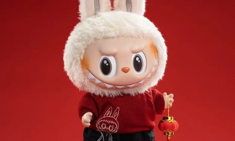 Boneco fofinho com capô de coelho, roupa vermelha e tênis, segurando lanterna de decoração.