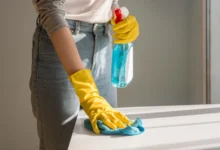 Mulher utilizando luvas amarelas e limpando superfície com pano azul, aplicando truques de limpeza eficientes em sua casa.