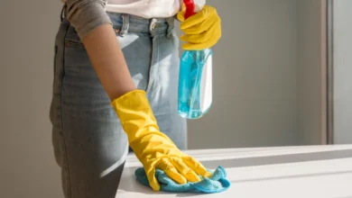 Mulher utilizando luvas amarelas e limpando superfície com pano azul, aplicando truques de limpeza eficientes em sua casa.