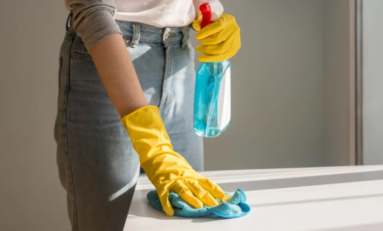Mulher utilizando luvas amarelas e limpando superfície com pano azul, aplicando truques de limpeza eficientes em sua casa.