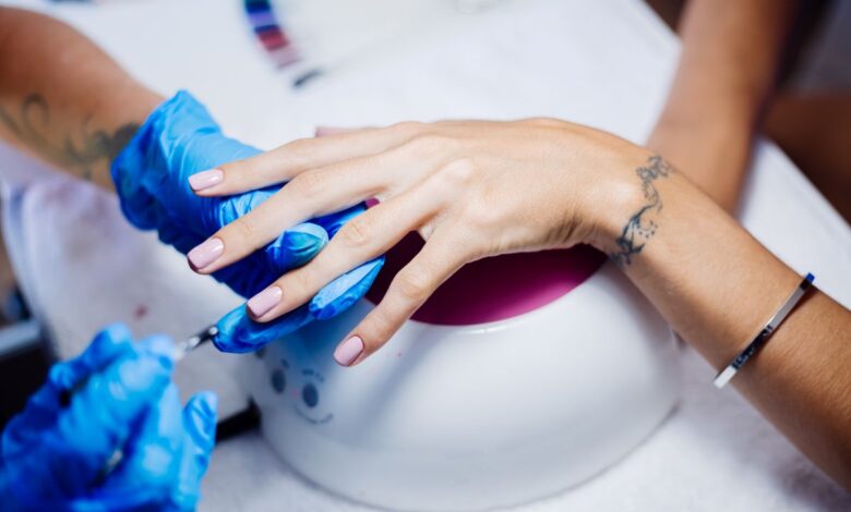 Manicure realizando cuidados em unhas de gel com luvas azuis