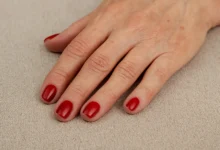 Mão de mulher madura com unhas pintadas de vermelho sobre tecido bege