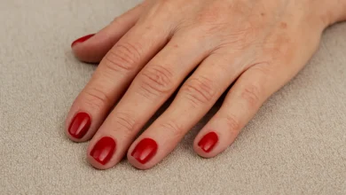 Mão de mulher madura com unhas pintadas de vermelho sobre tecido bege
