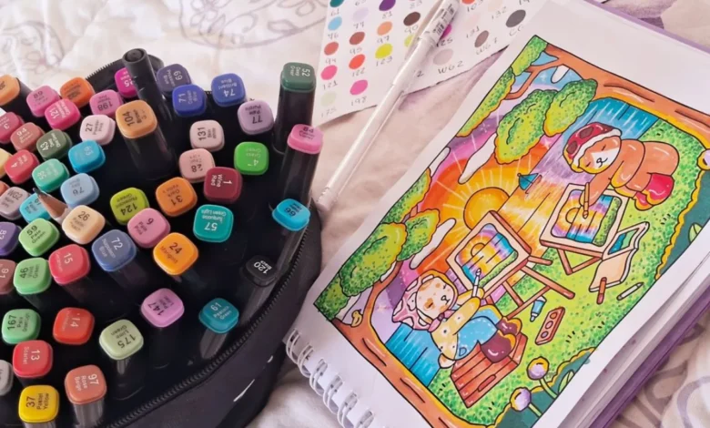 Kit de marcadores coloridos ao lado de um desenho Bobbie Goods colorido com ursinhos pintando ao pôr do sol.