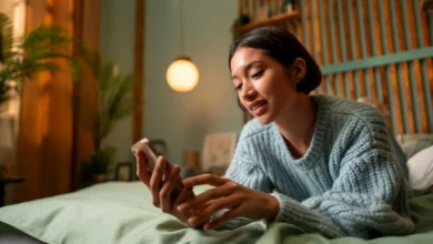 Mulher deitada na cama usando o celular com expressão tranquila