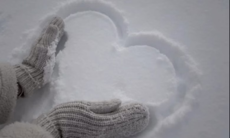 Desenho de um coração na neve feito com as mãos, simbolizando carinho e afeto em um dia frio