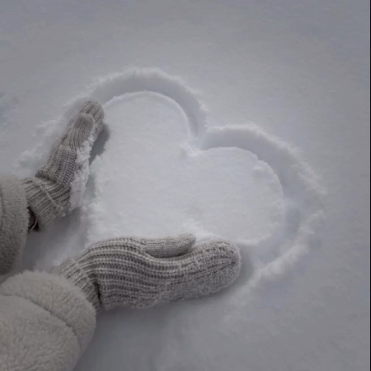 Desenho de um coração na neve feito com as mãos, simbolizando carinho e afeto em um dia frio