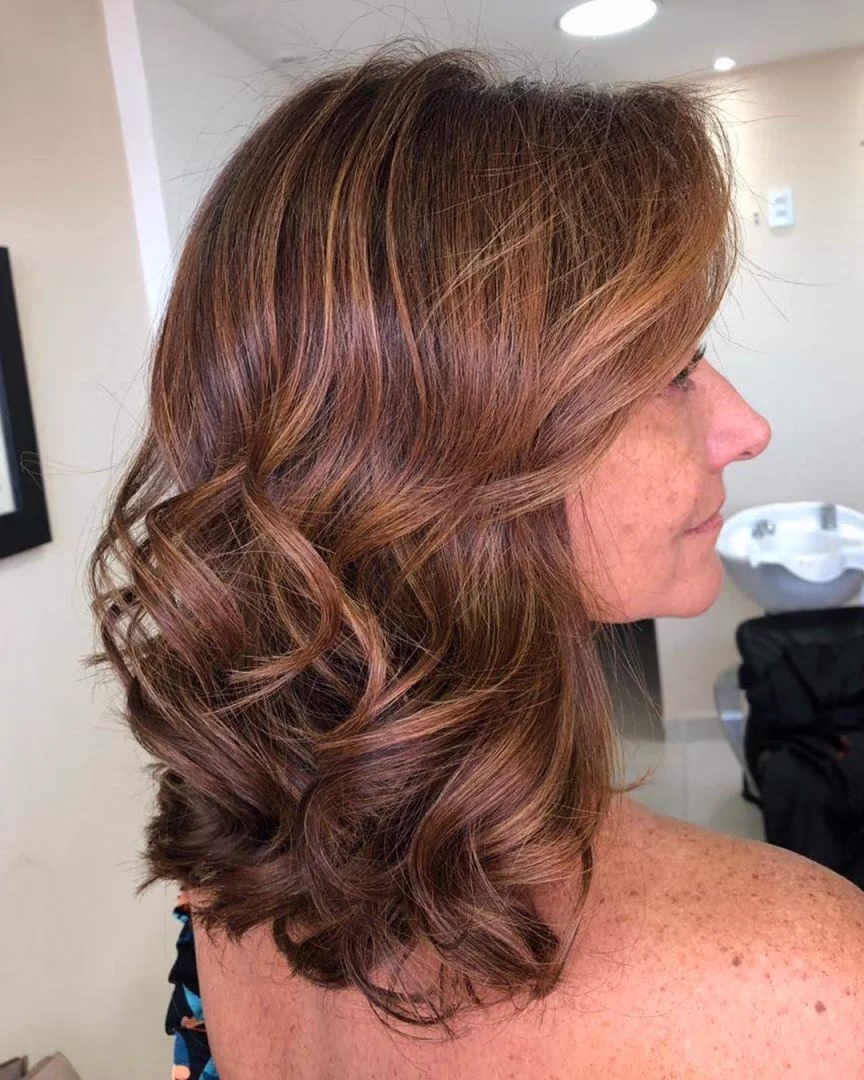 Mulher com cabelo morena iluminada, estilo natural e sofisticado, com ondas suaves e reflexos discretos de luz.
