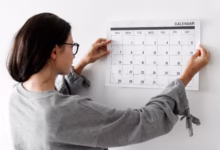 Mulher organizando um calendário de agosto de 2025, verificando datas comemorativas e feriados.