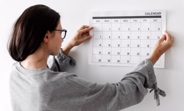 Mulher organizando um calendário de agosto de 2025, verificando datas comemorativas e feriados.