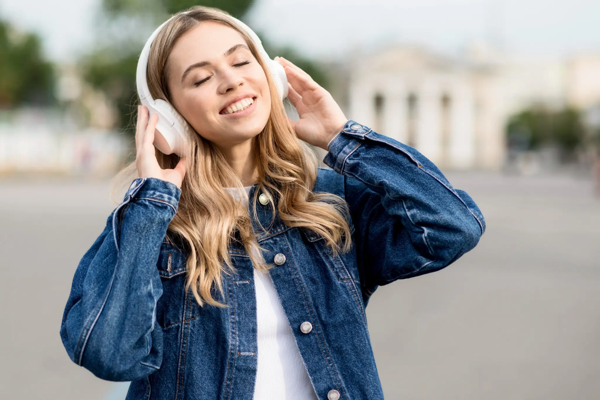 Mulher sorrindo enquanto ouve música com fones de ouvido, em ambiente ao ar livre