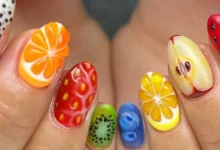 Unhas decoradas com frutas, mostrando nail art criativa com laranja, limão, kiwi, morango, maçã e melancia.