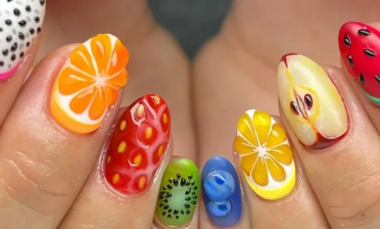 Unhas decoradas com frutas, mostrando nail art criativa com laranja, limão, kiwi, morango, maçã e melancia.