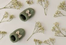 Par de sapatinhos de bebê em crochê verde com laço, cercado por flores delicadas