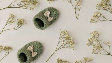 Par de sapatinhos de bebê em crochê verde com laço, cercado por flores delicadas