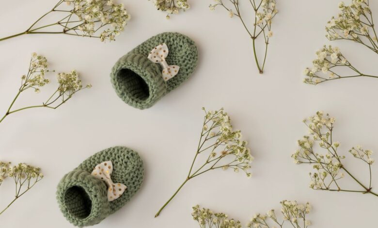 Par de sapatinhos de bebê em crochê verde com laço, cercado por flores delicadas