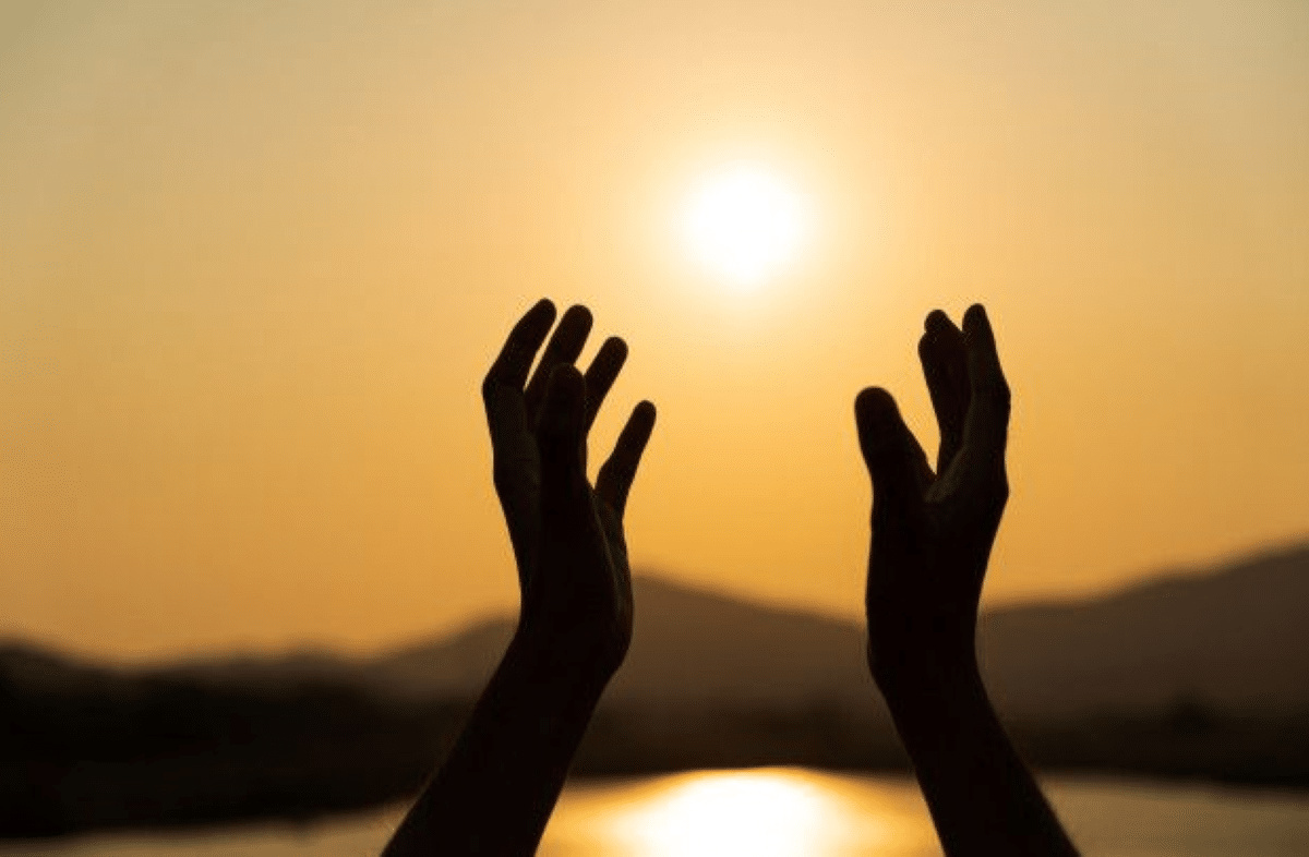 Mãos abertas ao sol, simbolizando a recepção de bênçãos para um mês de julho repleto de paz e esperança.
