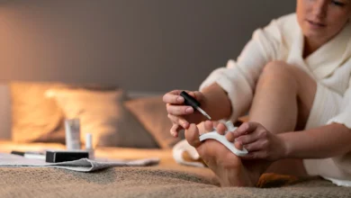 Mulher fazendo a pedicure em casa, aplicando esmalte nos pés com cuidado e conforto.