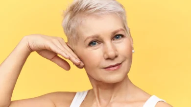Mulher madura com pele radiante tocando o rosto e sorrindo, refletindo os cuidados para manter a beleza depois dos 50 anos.