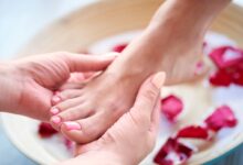 Massagem relaxante nos pés com unhas bem cuidadas e pétalas de rosa ao redor