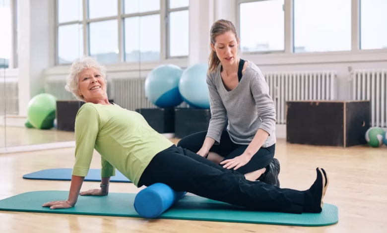 Idosa praticando pilates com auxílio de profissional em estúdio.