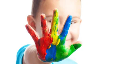 Criança autista sorrindo com a mão coberta de tinta colorida, representando a diversidade do espectro autista.