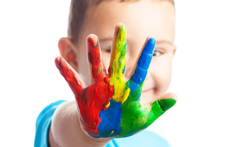 Criança autista sorrindo com a mão coberta de tinta colorida, representando a diversidade do espectro autista.