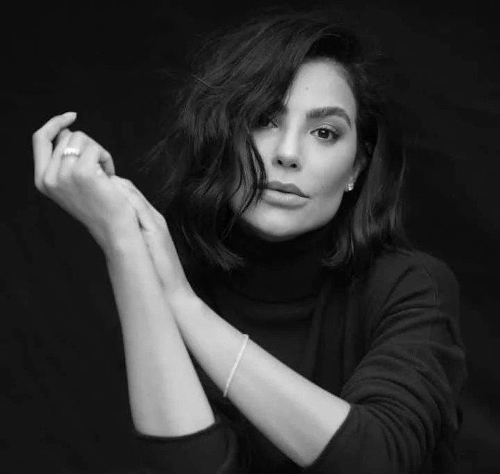 Mulher posando em foto preto e branco com o braço cruzado, olhando para a câmera.