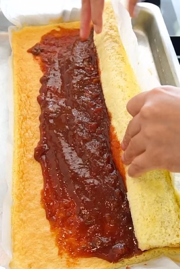 Preparando o rocambole doce, com recheio de goiabada sendo espalhado sobre a massa antes de ser enrolado.