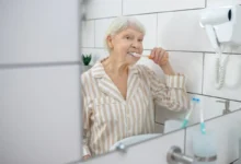 Idosa escovando os dentes em frente ao espelho do banheiro.