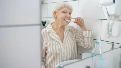 Idosa escovando os dentes em frente ao espelho do banheiro.