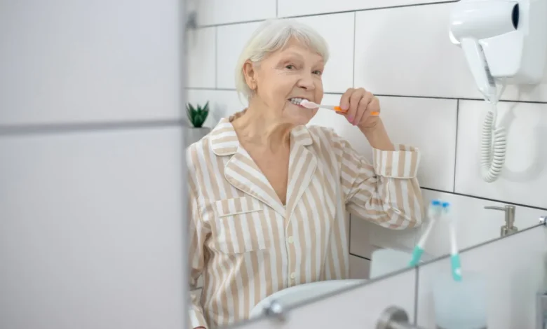 Idosa escovando os dentes em frente ao espelho do banheiro.