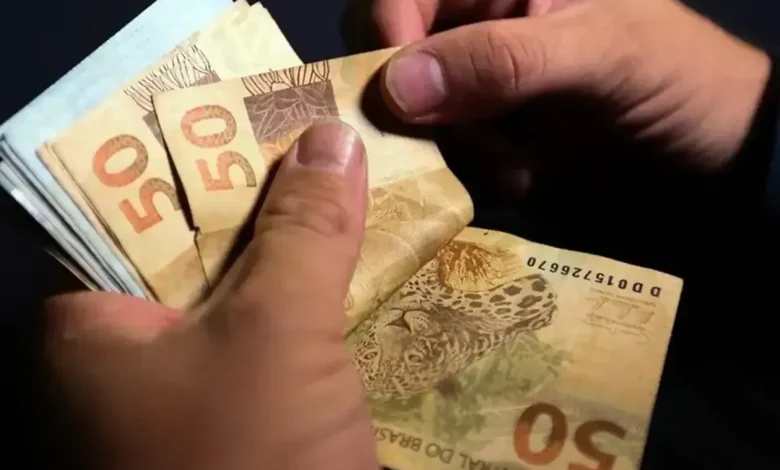 Pessoas contando notas de R$ 50, simbolizando o pagamento dos salários.