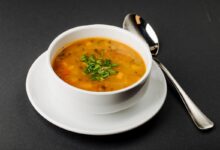 Caldo de mocotó servido em tigela branca com ervas frescas por cima