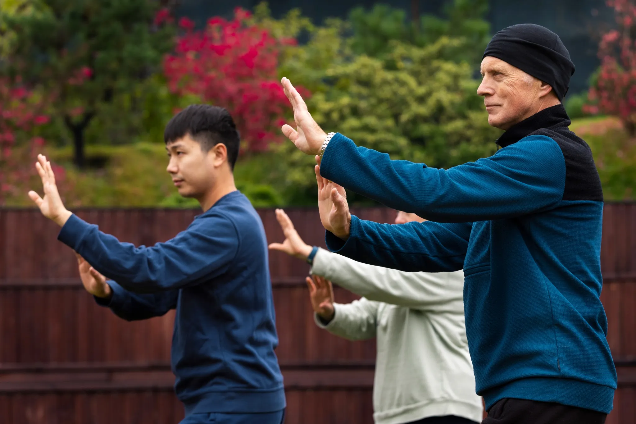 Grupo de pessoas praticando Tai Chi Chuan ao ar livre, com foco em movimentos suaves e controlados, adequado para idosos.