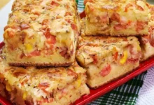 Fatias de torta salgada com queijo derretido, tomate, milho e uma crosta dourada sobre um prato vermelho.