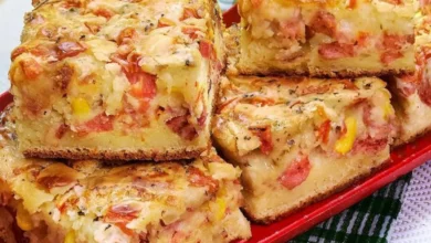 Fatias de torta salgada com queijo derretido, tomate, milho e uma crosta dourada sobre um prato vermelho.