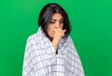 Mulher com tosse, coberta com um lençol xadrez, aparentando estar doente e desconfortável.